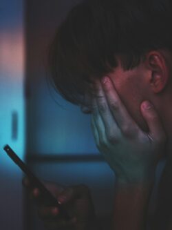 Man holding a mobile phone in one hand while covering his face with the other, appearing worried or frustrated.