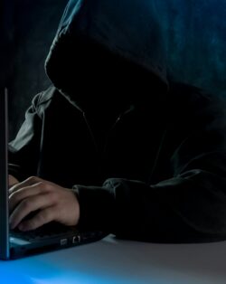 Man in black hooded jacket typing on a laptop. 