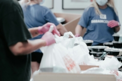 People wearing pink rubber gloves pack white nylon bags with donations to distribute to those in need.