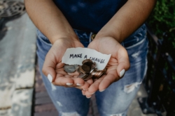 A woman wearing jeans holds both coins and a paper slice reading 'make a change' in her cupped hands, with her palms facing upwards.