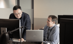 Two people in an office, smiling while collaborating and looking at a screen.