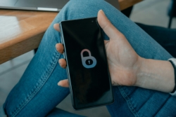 Close-up of a hand holding a smartphone resting on a denim-clad thigh, with a lock icon displayed on the screen, symbolising security and emphasising its importance.