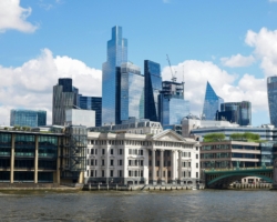 The London skyline featuring modern glass and metal skyscrapers in the City area, with a classical white building in the foreground.