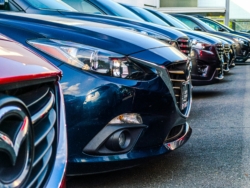 Row of red and blue Mazda 3 cars parked at a dealership in Fairfax, VA, with light reflecting off the vehicles.