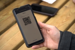 A person holding a smartphone displaying a screen from the Fire mobile application: a €5 open banking payment request with a QR code for the customer to scan and pay directly from their bank.