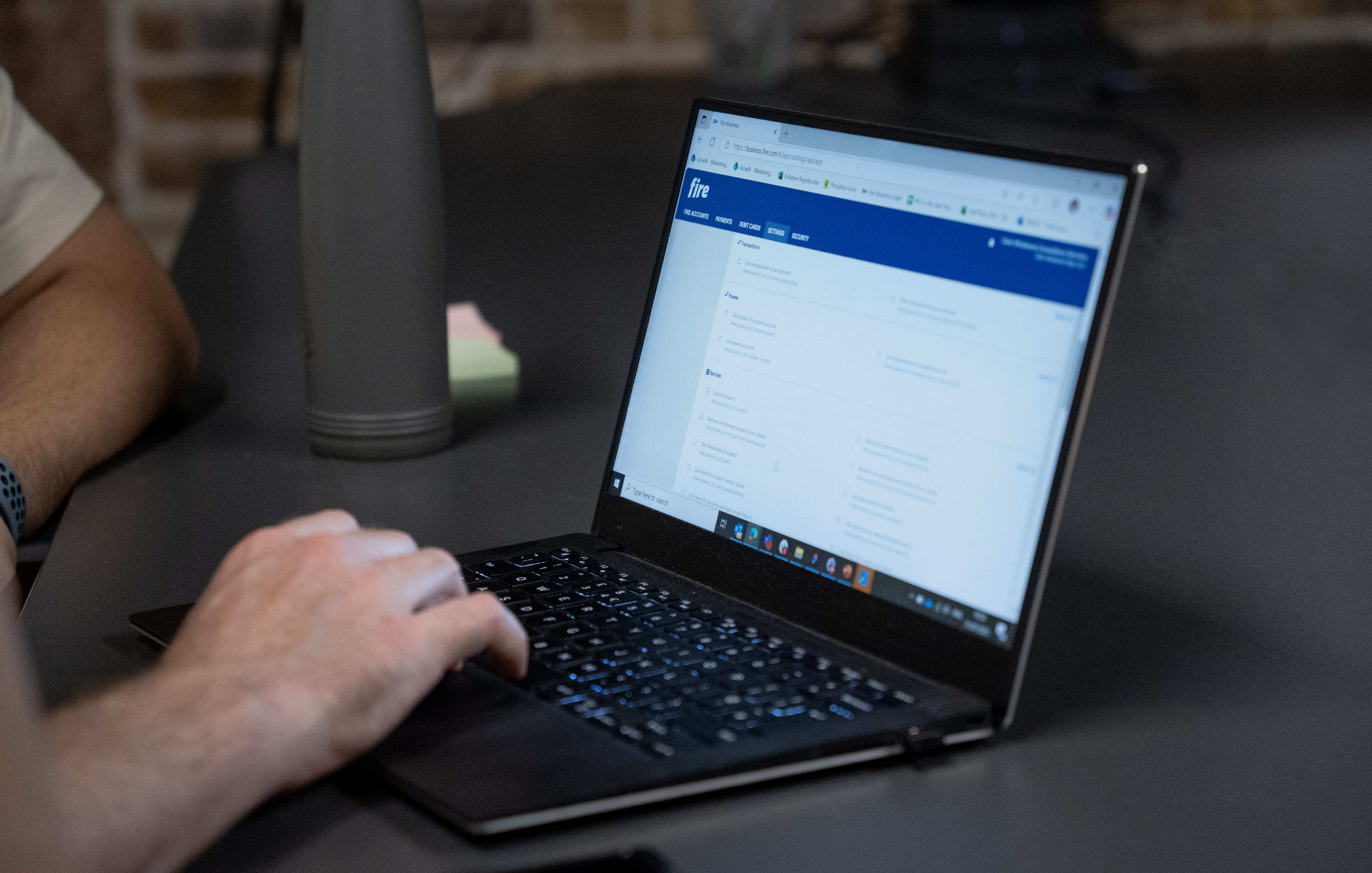 Close-up of a person using a laptop at a desk, showing Fire’s business account settings page with batch payment and payee settings visible on the screen.
