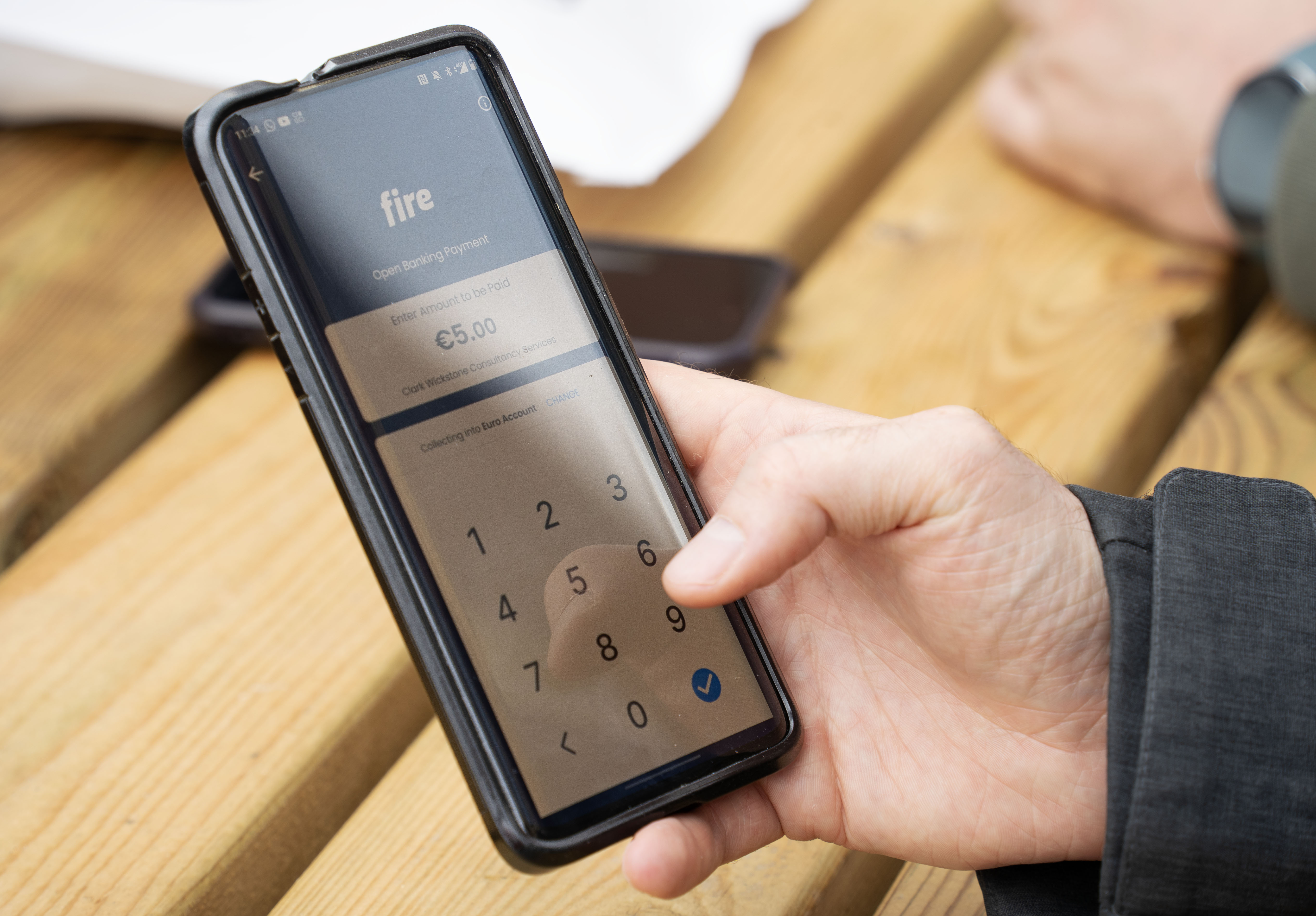 Person holding a smartphone displaying the Fire app while entering a €5 open banking payment.