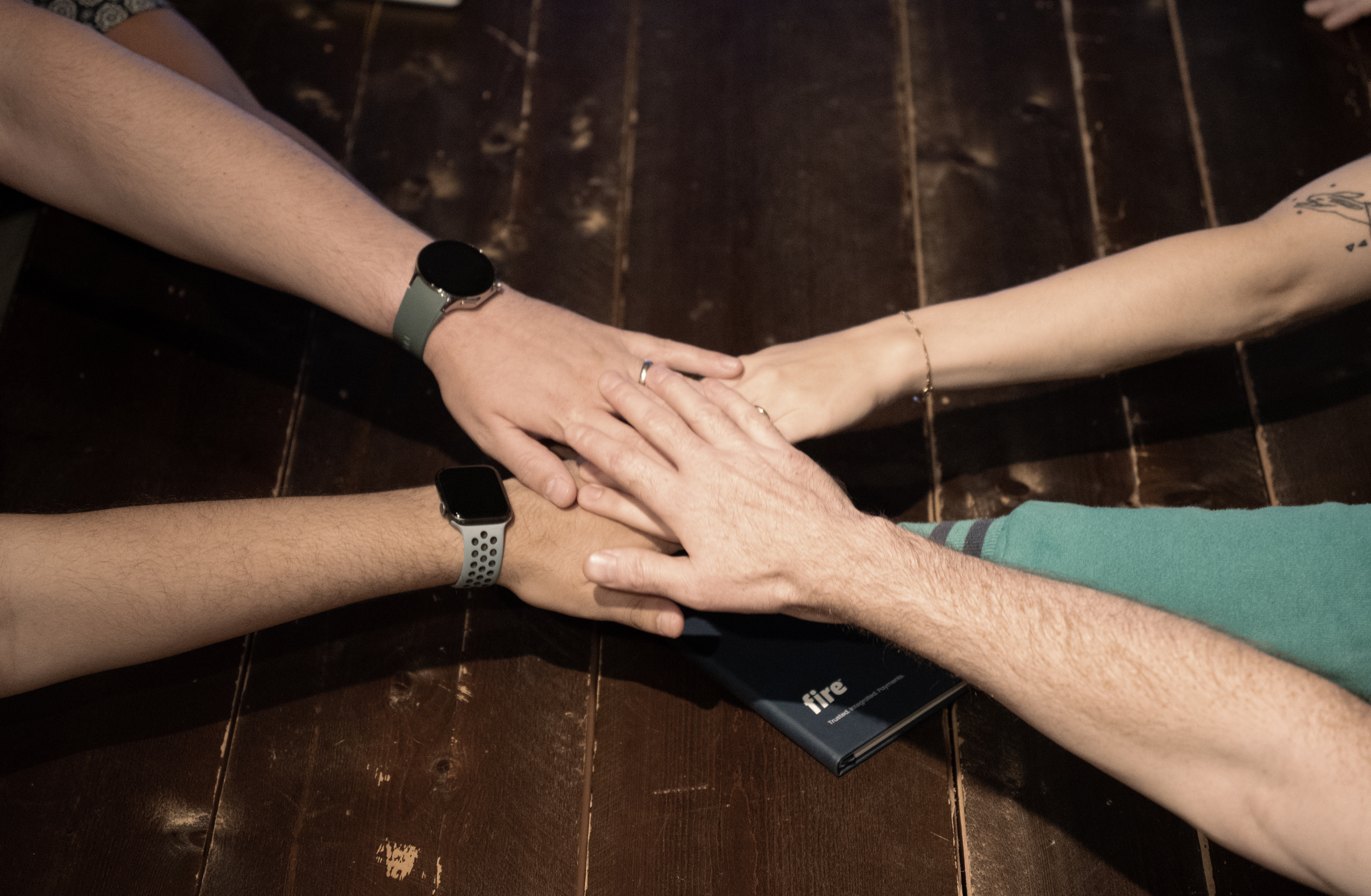 Several people placing their hands together in the centre of a wooden table.