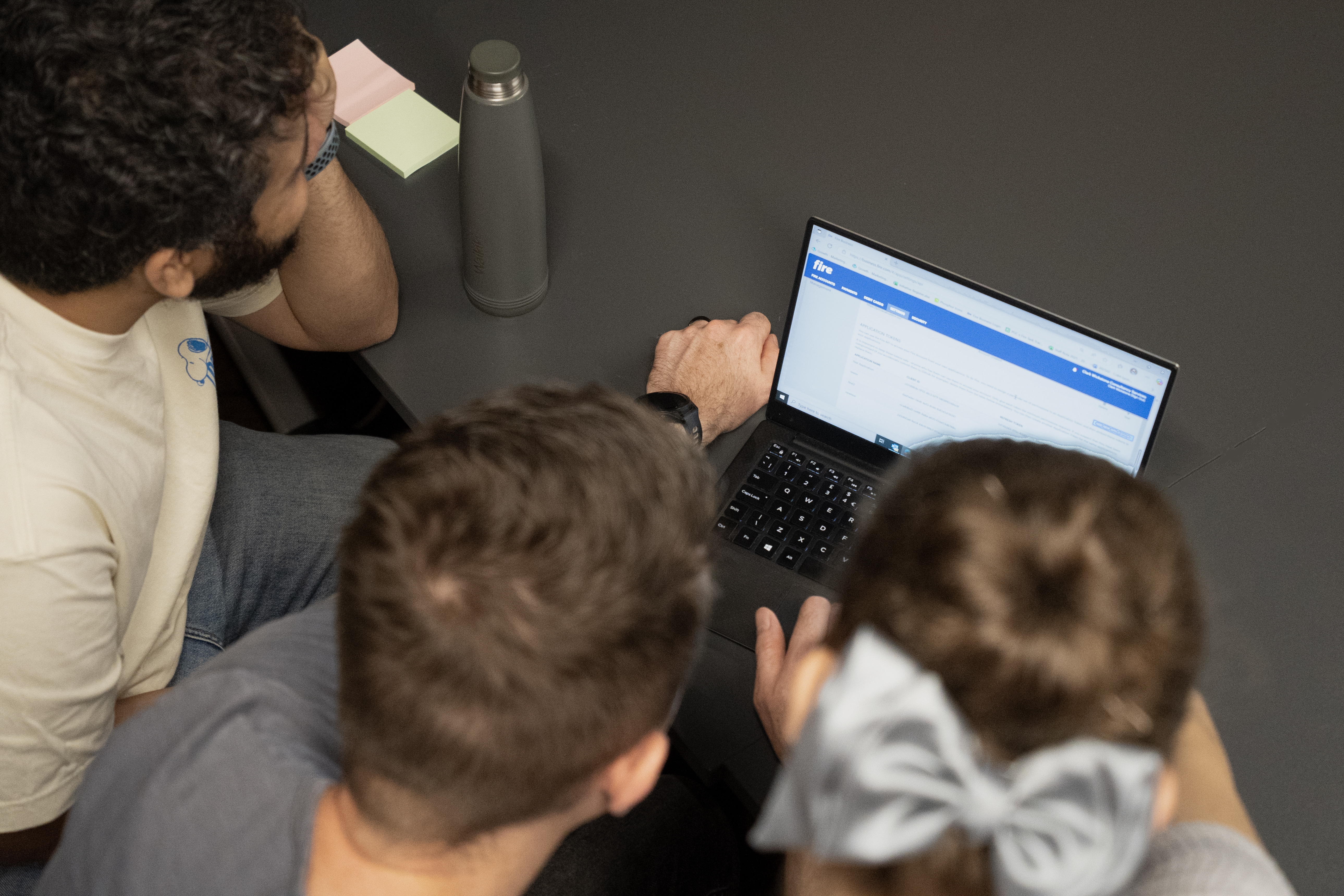 Three people looking at a laptop screen on a table.