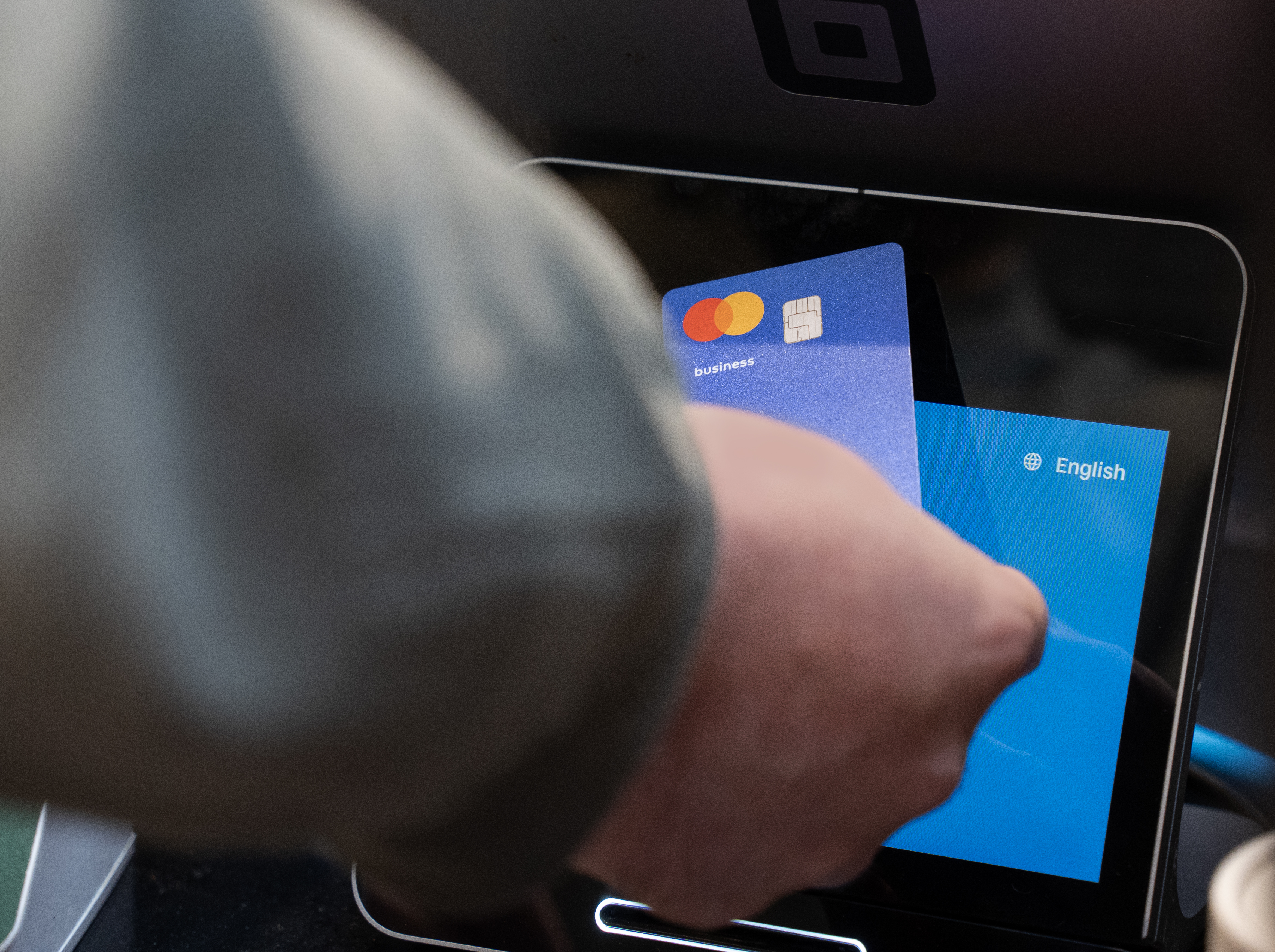 Person using a business payment card at a self-service checkout screen.