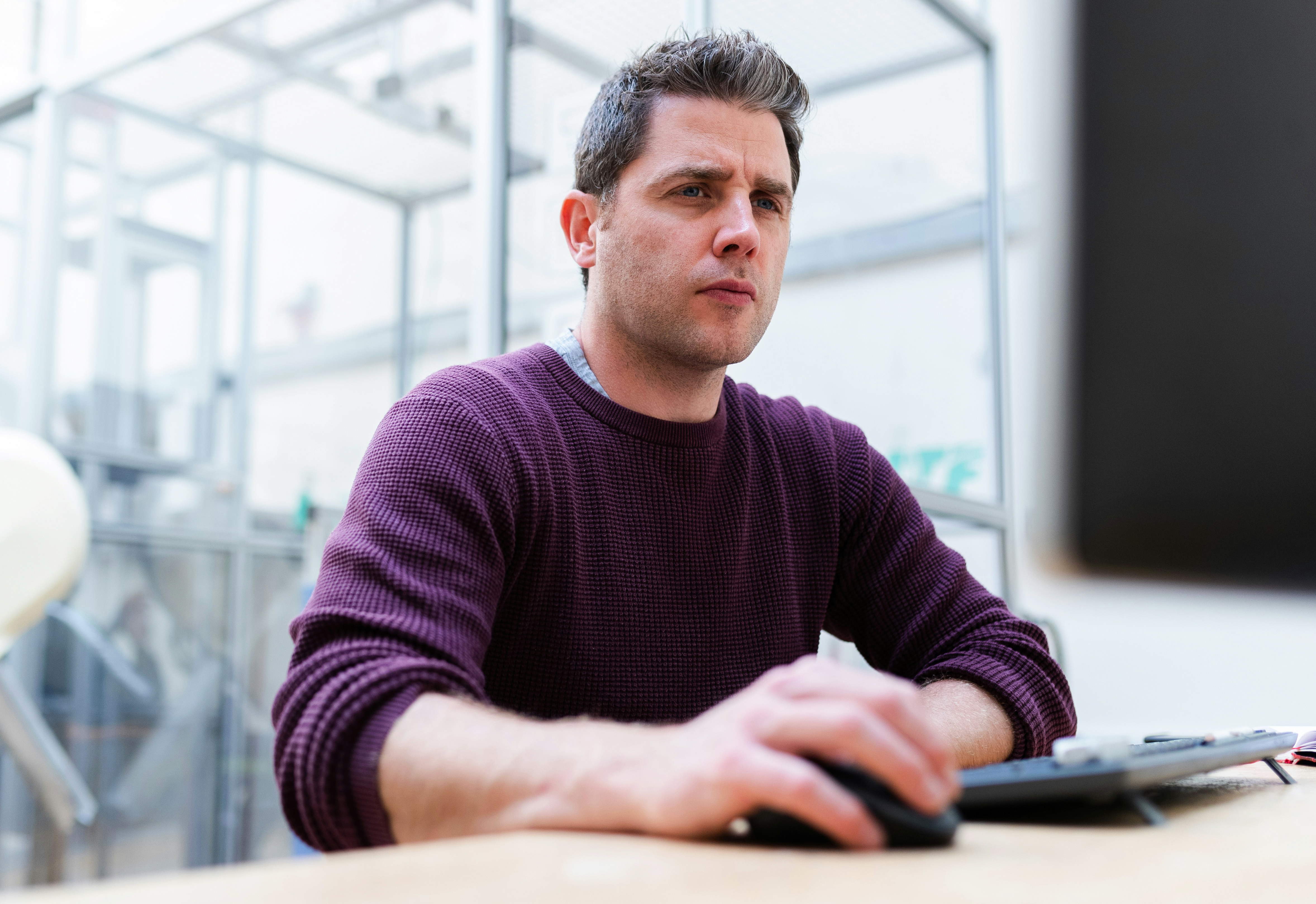 Man looking pensive at a computer screen, frowning while holding a mouse.