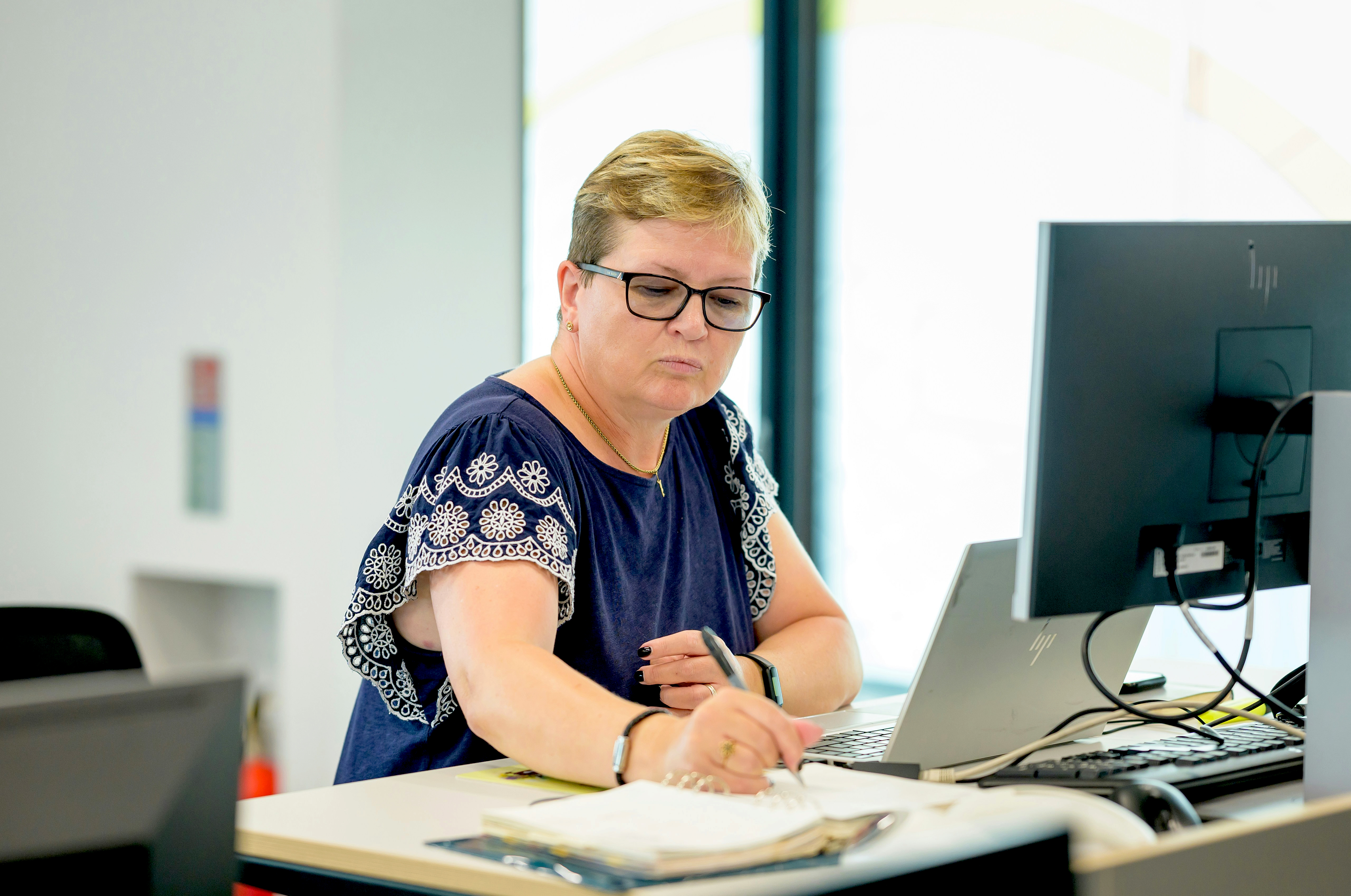 A woman working at a desk with a laptop and computer monitor.