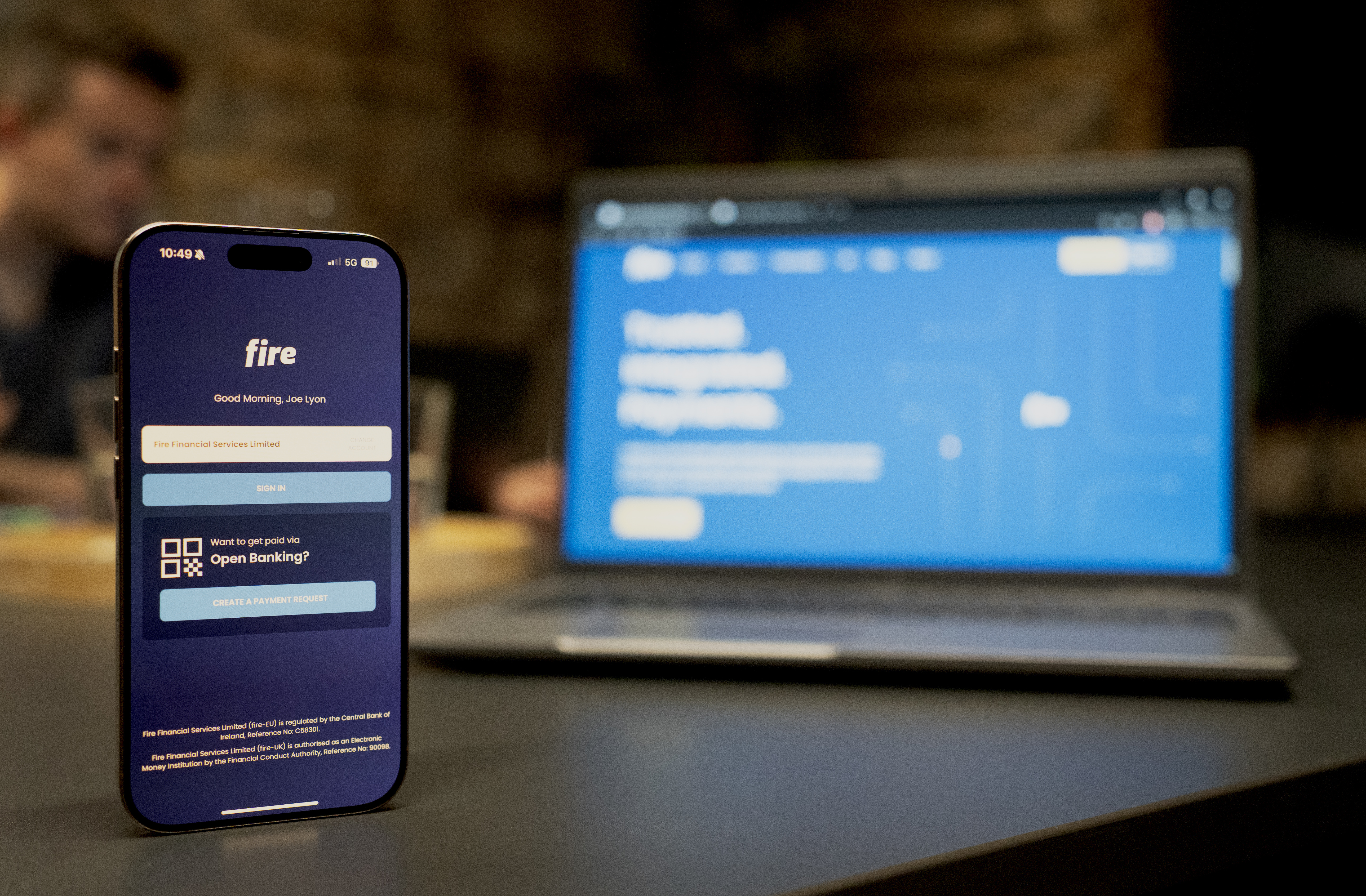 Phone showing Fire’s login, with a laptop showing Fire’s website in the back.